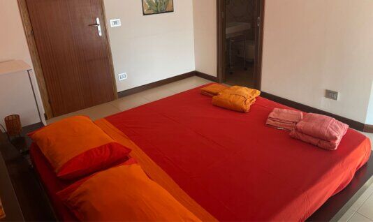 Camera con letto matrimoniale e biancheria rossa e arancio